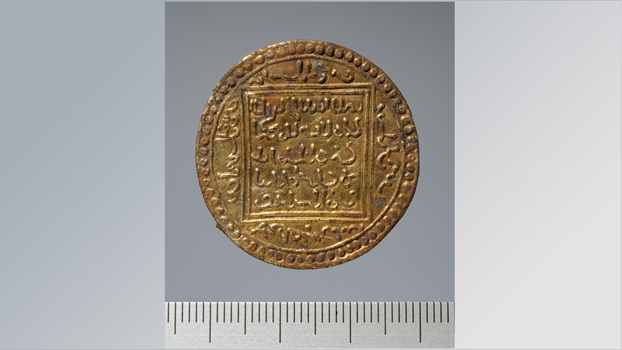 Die vergoldete Pseudomünzfibel. Es handelt sich um die Nachahmung einer islamischen Münze, eines almohadischen Gold-Dinars, der in skandinavischer Tradition zu einer Gewandschließe (Fibel) umgearbeitet worden ist.