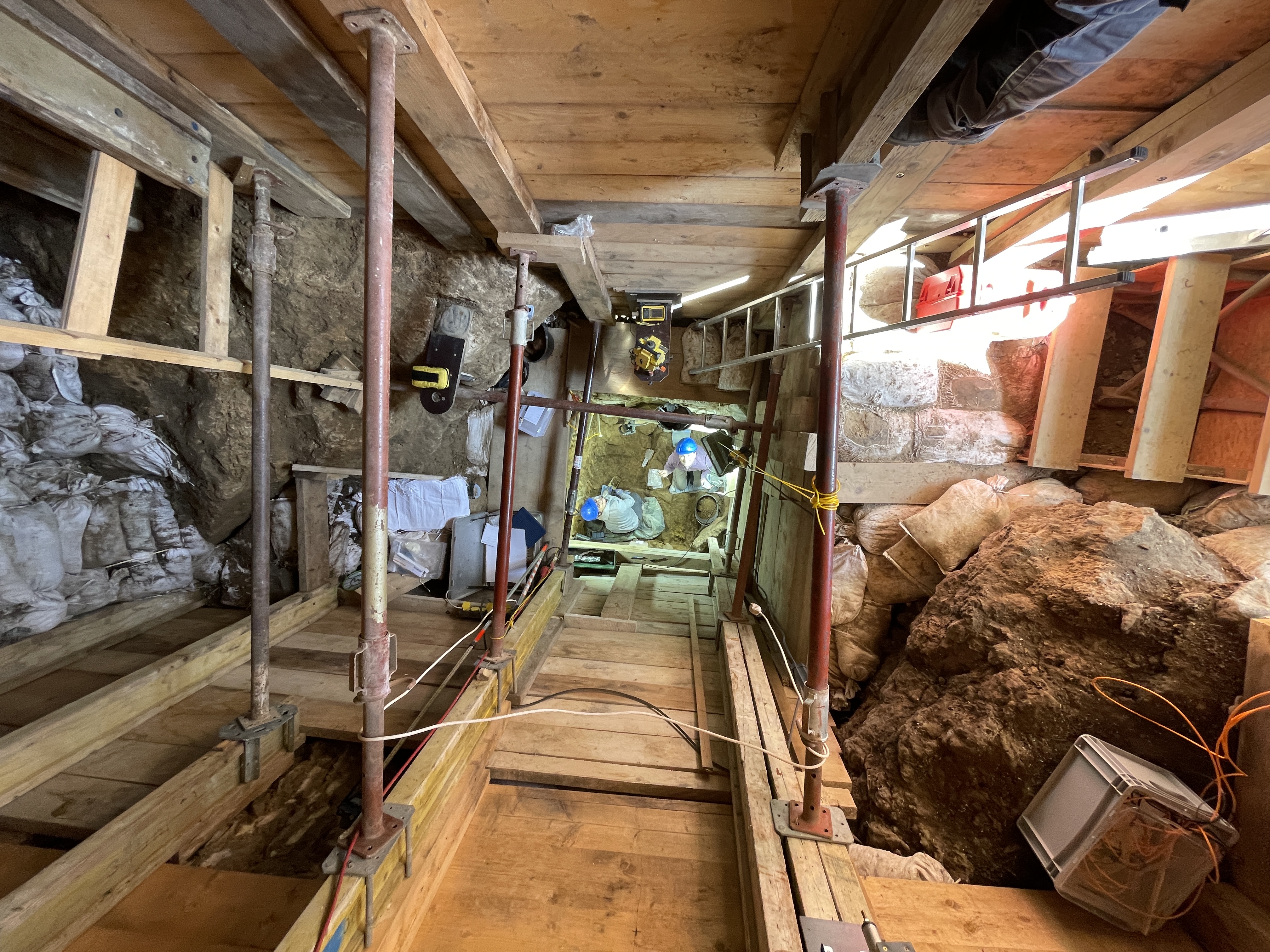 Das Foto zeigt den senkrechten Schacht der Ausgrabungen in der Ilsenhöhle in Ranis. Der Schacht ist komplett mit Holz ausgezimmert um ihn zu stützen. Man blickt 8 m nach unten, wo Archäologen die Ausgrabung durchführen.